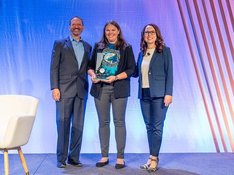 Alison Colotelo being presented a trophy for the award on a stage standing between two officials from National Hydropower Association