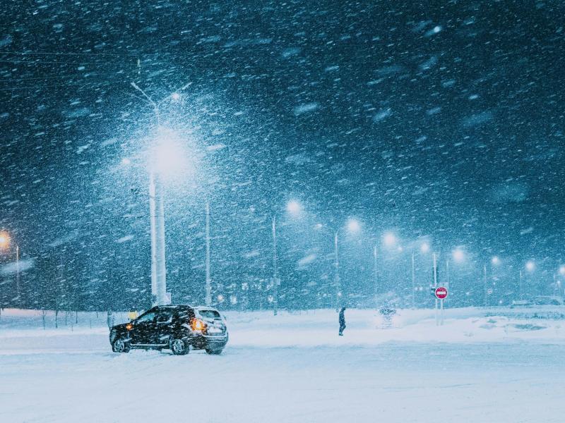 Photograph shows a parking lot bordered by street lamps, during a snow storm. 